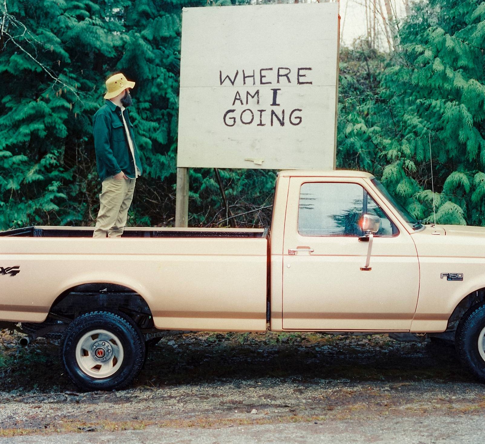 Jess Sloss standing in the bed of a pickup beneath a hand-painted 'Where Am I Going' sign